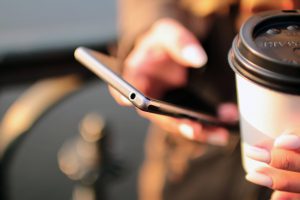 Woman texting with cup of coffee in hand